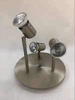 Brushed metal ceiling fixture with three adjustable spotlight heads on a round base, shown from a front angle.