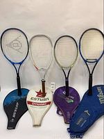 Four tennis rackets displayed upright against a white background with their respective cases laid in front below each racket. Cases are soft, zippered, and brand marked.