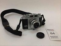 Front view of vintage Balda Werk Bunda camera with attached black neck strap and lens cap placed nearby.