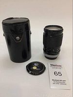 Image showing Canon FD 135mm f/2.5 S.C. lens standing upright with front lens cap and black carrying case beside it.