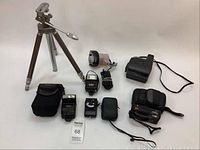 Photo showing a vintage tripod, multiple small camera bags, two flashes, a handheld light meter, small battery-powered fan, and accessory pouches.