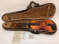 Open black hardshell case containing violin, bow, instruction booklet and rosin block