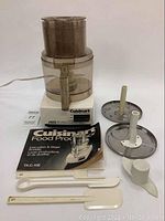 Front view of Cuisinart DLC-10E food processor with accessories and manual arranged in front on white background.