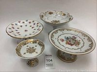 Full view of four vintage porcelain cake stands and pedestal dishes showing floral patterns and gold trims.