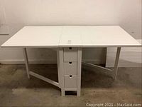 Front view of IKEA Norden white drop leaf table fully extended showing top surface and drawer column.