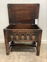 Front view with the lid open showing interior storage compartment and decorative front panel with arch carvings