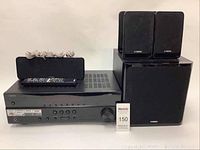 Front-on view of AV receiver with center speaker, remote control, coiled speaker wire on chassis and two satellite speakers atop the subwoofer.