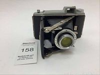 Front view of Kodak Tourist folding camera with lens, bellows, and viewfinder visible, alongside MaxSold tag.