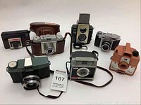 Lot of seven vintage cameras displayed on table, variety of models and styles visible