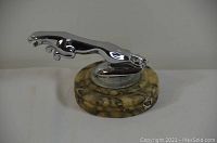 Front view of the chrome Jaguar hood ornament mounted on the round marble base, showing the detailed leaping jaguar figure and the textured marble surface.