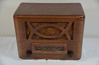 Front angle view of vintage wooden tabletop radio showing wood casing, grille and tuning dial with knobs.