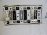 Front view of the rectangular tray showing atomic starburst pattern in vertical bars of black, gray, white, and gold.