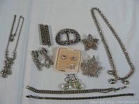 Photo showing multiple silver-tone rhinestone jewelry pieces including necklaces, earrings, brooches, and bracelets on white background.