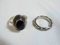 Two sterling silver rings on white background, one with black stone and one twisted band.