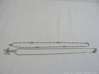 Two silver necklaces laid flat showing one with blue stone turtle pendant and one plain with silver beads