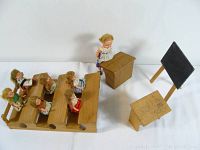 Overview of entire classroom setup with dolls on benches, teacher at desk, chair, and blackboard visible