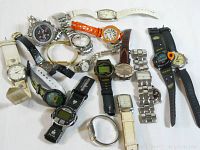 Overview of 16 assorted watches in various styles and colors laid out on white surface