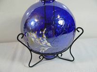Front view of blue glass globe oil lamp sitting on a black metal stand, showing crackled glass texture and floral designs.