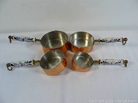 Photo showing all four copper measuring cups with ceramic floral handles arranged side by side.