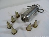 Photo shows vintage metal cake decorating syringe with seven assorted metal tips arranged on a white background.