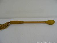 Full view of an indigenous drum beater showing wooden handle with suede padded beater end and leather fringe tassels at the other end.