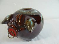 Side view of brown and blue glazed ceramic piggy bank shaped like a pig, showing curved body and coin slot on top.