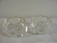 Pair of two clear textured glass candle holders with Arabia Finland logo stickers on each, viewed side-by-side from an angle showing shape and texture.