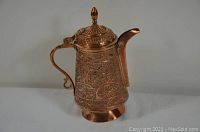 Front view of antique decorative copper pot showing detailed embossing and curved spout.