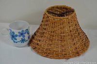 Side view of conical wicker lamp shade next to coffee mug for size reference.