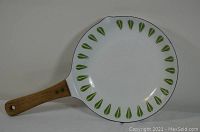 Enameled pan top side showing white background with green leaf pattern around edge and wooden handle.