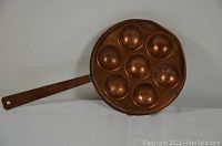Front top view of the copper egg pan showing 7 rounded egg molds and handle.