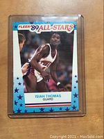 Front view of 1989 Fleer All-Stars Isiah Thomas basketball card in protective plastic sleeve on wooden background.
