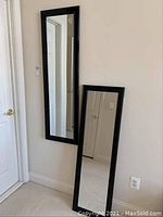 Photo showing two black framed rectangular mirrors placed near a wall and door.