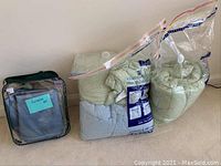 Two vacuum-sealed plastic bags containing light green and light blue bedding items, labeled as comforters and bedspread.