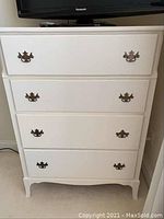 Front view of a white four drawer dresser with decorative metal handles and curved leg design.