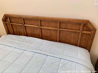 Front view of wooden headboard mounted on bed with light blue comforter partially visible.