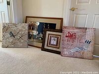 Four framed artworks leaning against wall on carpeted floor, showing variety and condition of pieces
