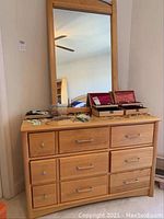 Front view of the chest with mirror mounted above, showing the wood finish, drawer handles, and items on top.