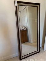 Full view of mirror leaning against wall, showing entire frame and reflective surface