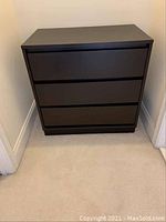 Photo of dark wooden chest of drawers with three drawers in corner of room.