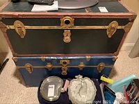 Front view of two stacked vintage steamer trunks showing green and blue trunks with metal hardware and leather handles