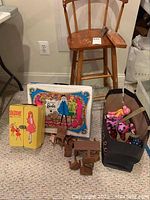 Photo showing vintage wooden high chair, Barbie doll case, Skipper doll box, stuffed animals in carrier bag, small wooden table and toy chairs on carpeted floor