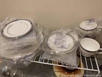 Photo displaying wrapped assorted plates and cups including large and small plates, saucers, and cups in Amherst design.