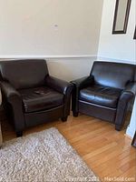 Pair of dark brown Palliser leather armchairs displayed side by side in a room with hardwood flooring and a white rug in front.