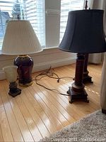 Photo of four table lamps of varying sizes, two with wood bases and cream shades, one small lamp with green frosted glass shade, and one medium ceramic-based lamp with cream fabric shade.