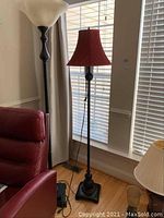 Two floor lamps side by side near a window. One has a frosted glass bowl shade, the other a red fabric bell shade.