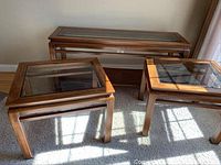 Three tables shown together including sofa table and two end tables with glass tops and wood frames.