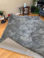 View of the full gray shag rug spread out on hardwood floor, showing texture and backing corner folded up.