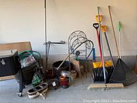 Image showing yellow-handled shovels, broom, rakes, metal flag stands, various pots, and gardening accessories grouped together.