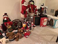 Overview of all Christmas decorations including figurines, plush toys, mugs, wreath, pillow, napkins, and stuffed animals arranged on carpet.